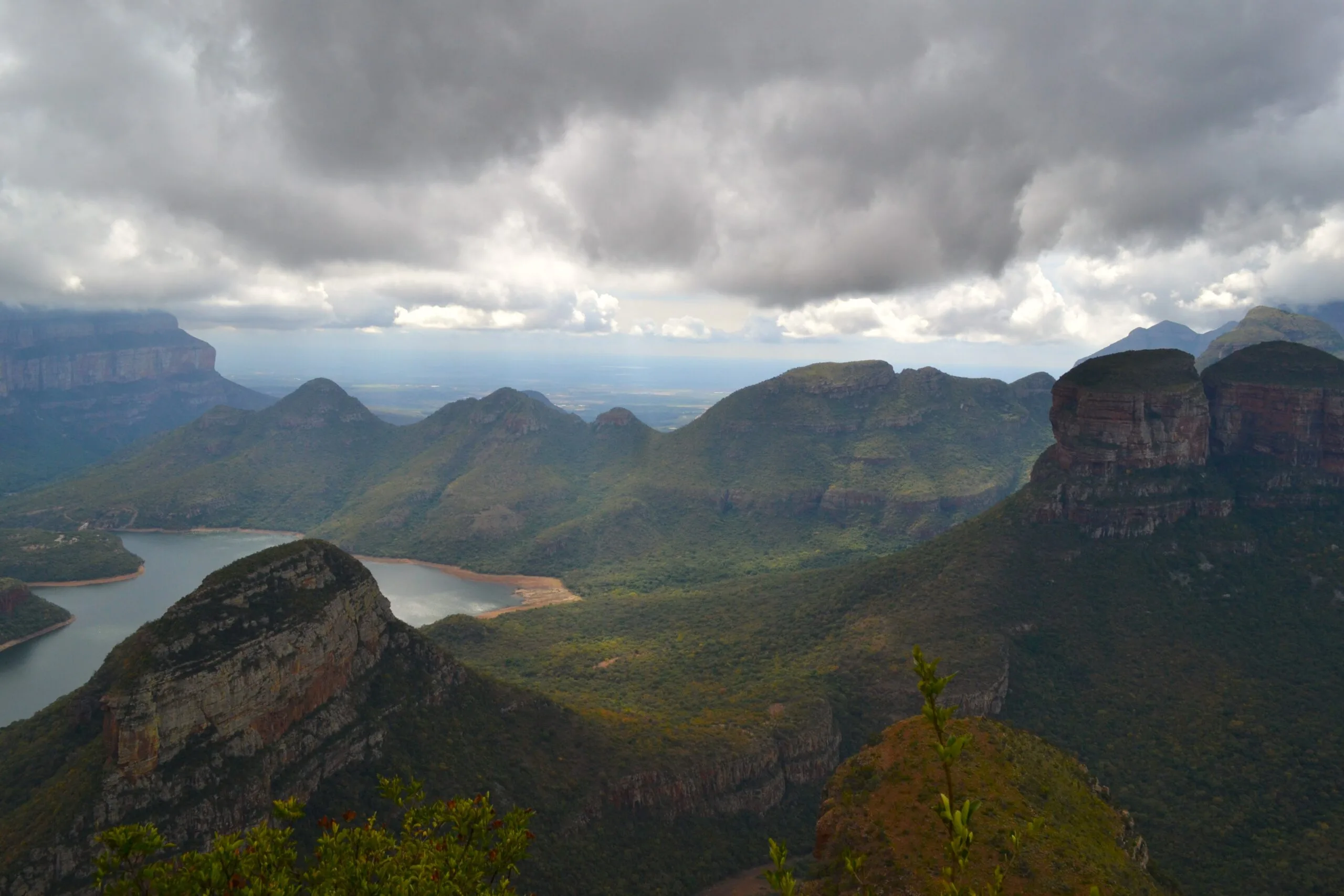 View from a mountain top looking down into the Blyde River Canyon in Mpumalanga — lush green subtropical vegetation covers the valley walls and a wide river winds far below